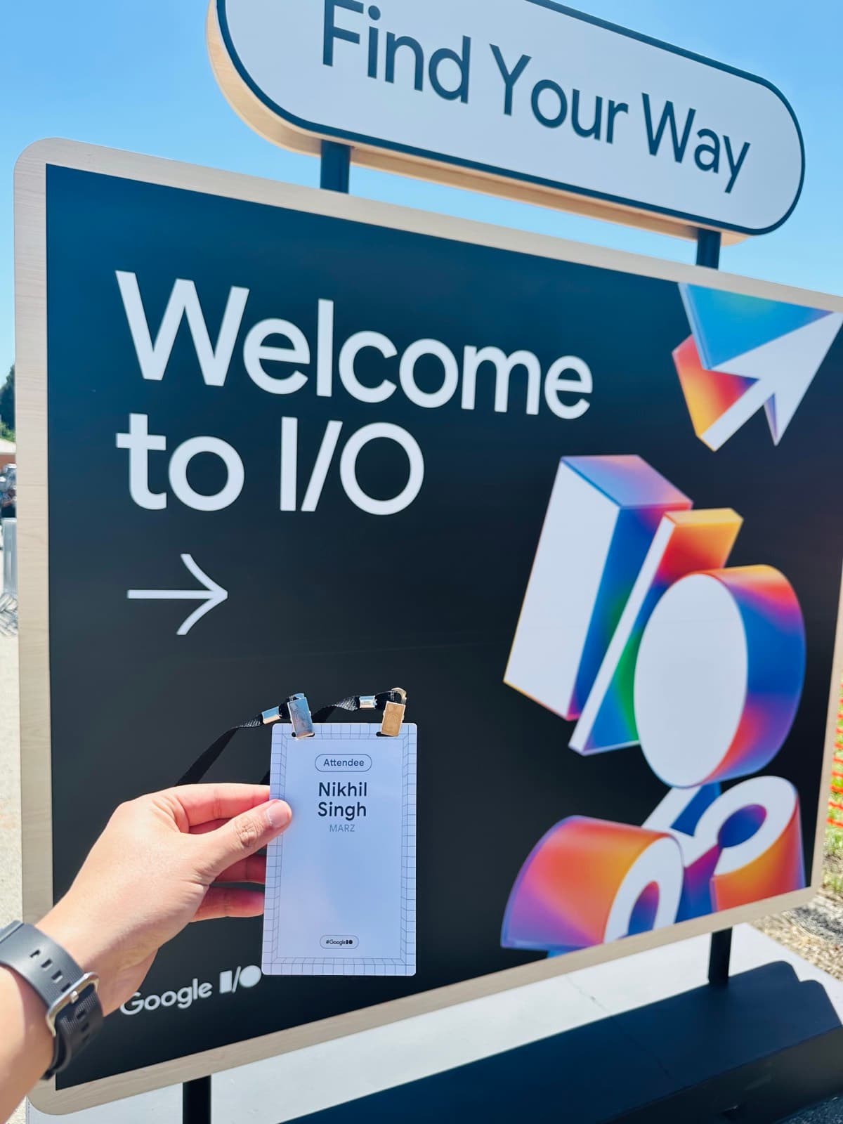 Attendee badge held up in front of the Welcome to I/O sign at Shoreline